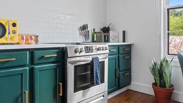 Una cocina con armarios verde azulado, una estufa blanca y un ventanal con vistas a la vegetación.