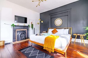 Une chambre à coucher avec un lit, une cheminée, un téléviseur et un grand miroir rond accroché au mur.