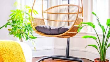 Una habitación de esquina con una silla colgante, una planta en maceta y un plaid amarillo.