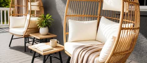 Dos sillones de mimbre con cojines, una mesita con un libro y una taza, y una planta en maceta.