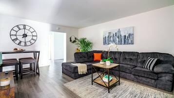 En moderne stue med en mørk sofa, et sofabord og et bybillede som maleri.