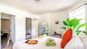 A neatly arranged bedroom with a bed, a bedside table with a plant, a mirror, and a window with natural light. - Jungle House Modern Lofts – Arena District & Short North (Columbus)