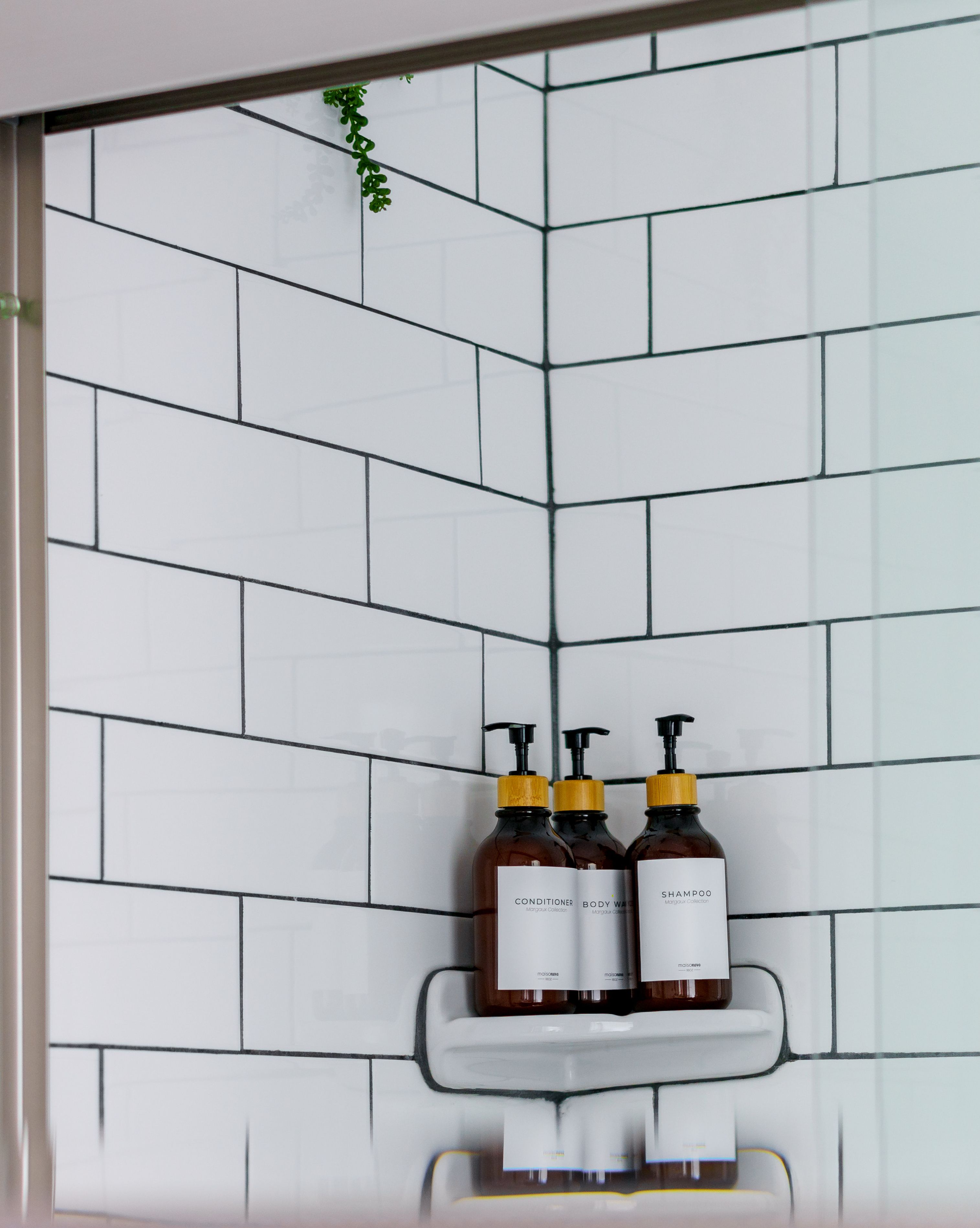 A bathroom with white tiled walls and a shelf holding two bottles of shampoo and conditioner.