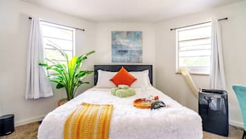 A neatly arranged hotel room with a large bed, a potted plant, a painting, and a window with curtains.