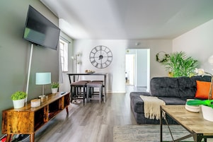 Una sala de estar moderna con un televisor de pantalla plana, una zona de comedor con una mesa y sillas, un gran reloj de pared y un sofá acogedor.