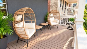A wooden deck with wicker chairs and a small table, surrounded by potted plants. - Jungle House Modern Lofts – Arena District & Short North (Columbus)