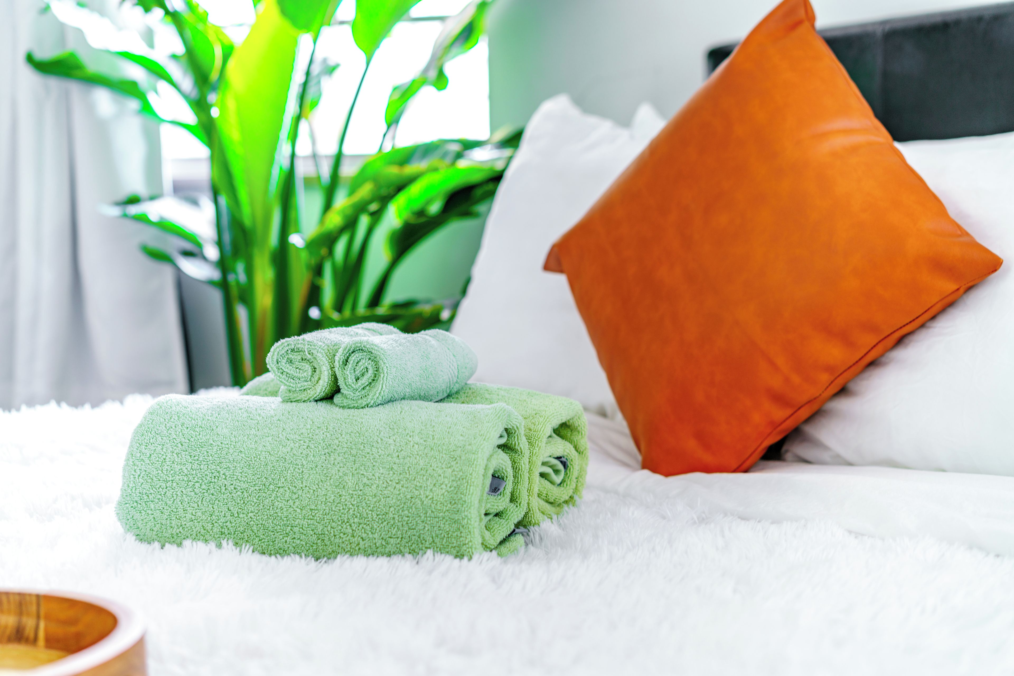 A neatly made bed with green towels, an orange pillow, and a white fluffy blanket.