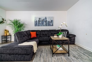 Ein modernes Wohnzimmer mit einem Ecksofa, einem Couchtisch und einem Stadtbild an der Wand.