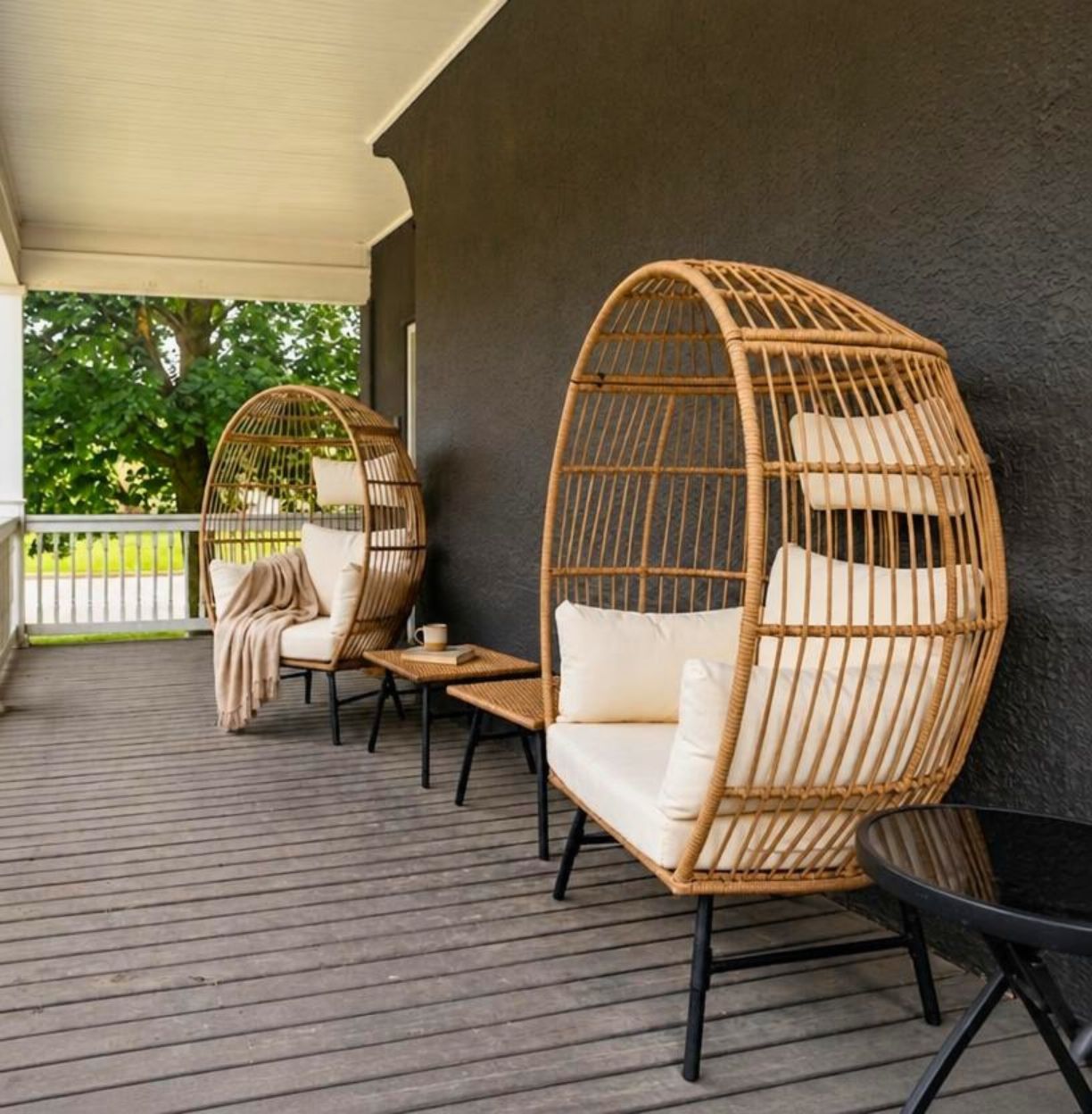 A covered outdoor seating area with wicker chairs and a sofa, a small table, and a black table.