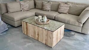 Ein beiges Ecksofa mit gemusterten Zierkissen, ein Couchtisch aus Holz mit Dekoration und ein Marmorboden.