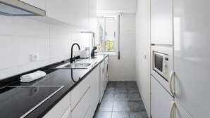 Una cocina moderna con armarios blancos, encimera negra, horno empotrado y ventana que proporciona luz natural.