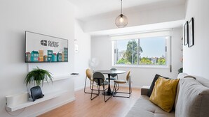 Una sala de estar moderna con un sofá, una mesa de comedor con sillas, un televisor montado en la pared y un amplio ventanal con vistas a la ciudad.