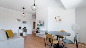 Una sala de estar moderna con un sofá gris, una mesa de comedor redonda con sillas, un ventilador blanco y un cartel en la pared que dice 'GUEST READY'.