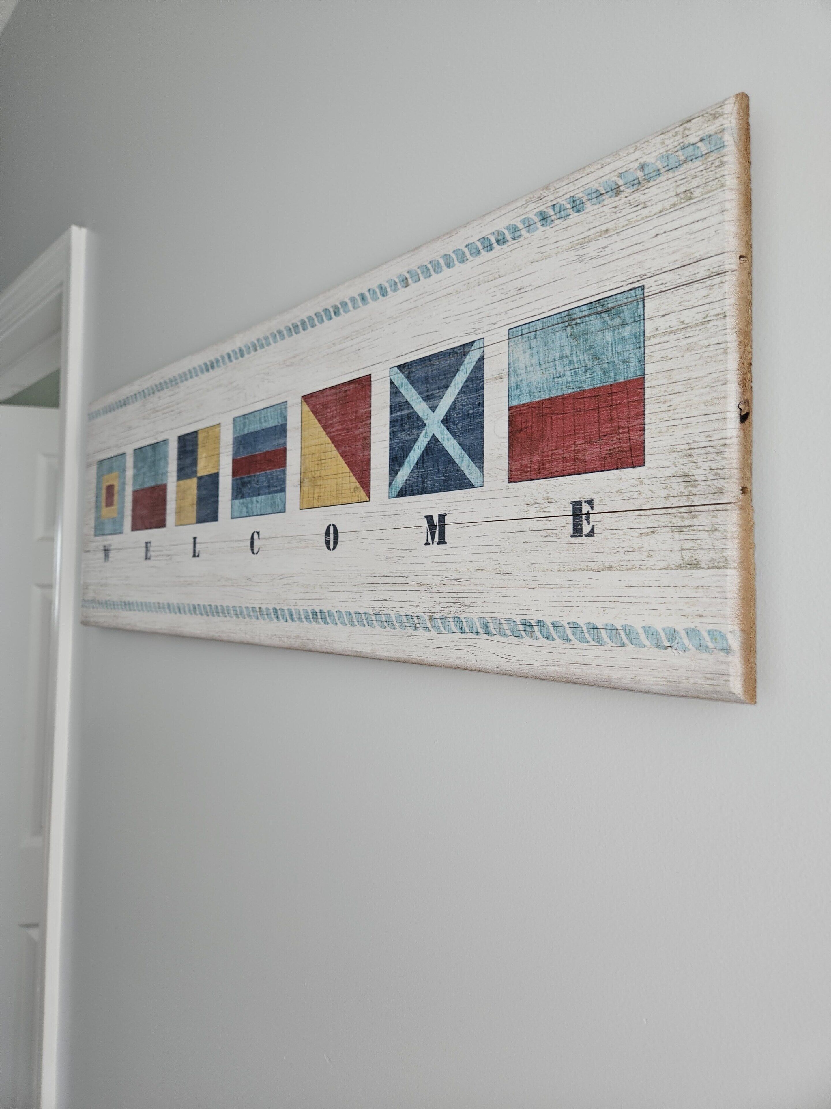 Ein an der Wand befestigtes Willkommensschild im rustikalen Stil, mit einer Reihe farbiger Quadrate und dem Wort 'WELCOME' in fetten Buchstaben.
