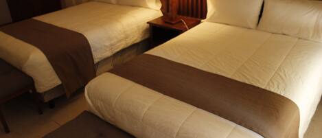 Una habitación de hotel con dos camas, una mesita de noche con lámpara y un banco.