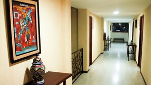 Un pasillo de hotel con un cartel enmarcado, un jarrón decorativo y un banco.