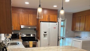 Una cocina con gabinetes de madera, un refrigerador de acero inoxidable, un microondas, una estufa, un lavamanos y un taburete de bar.