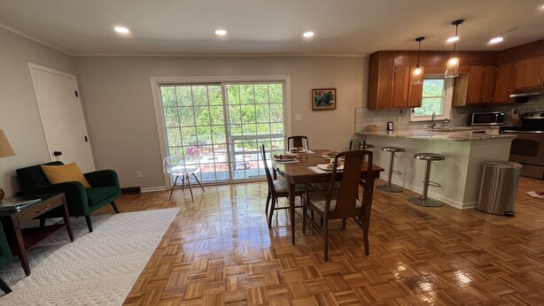 Una cocina amplia con piso de madera, un comedor con mesa y sillas, y un gran ventanal corredero que da a un patio.