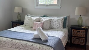 Un dormitorio con una cama, dos mesitas de noche, un ventilador de techo, una ventana y vistas al exterior.