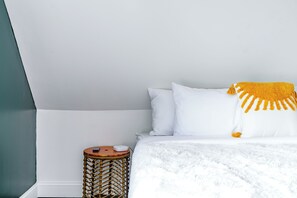 A bedroom with a bed, white pillows, a white blanket, a small round wicker side table, and a yellow throw blanket. - Jungle House Urban Lofts - Short North & Convention Center (Columbus)