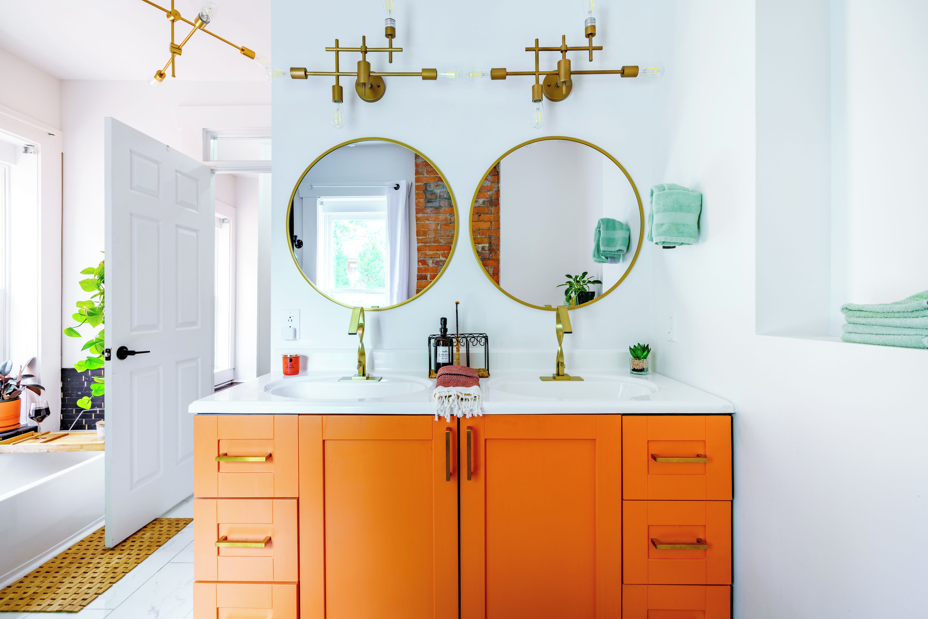 A bathroom with two round mirrors, an orange vanity, a white sink, and a door leading to another room.