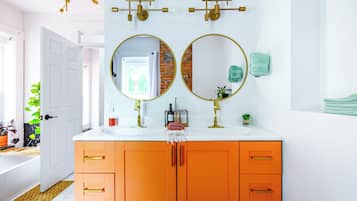 A bathroom with two round mirrors, an orange vanity, a white sink, and a door leading to another room.