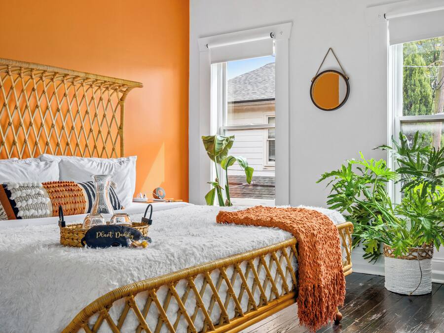 A bed with a white fluffy cover, a woven headboard, and a bedside table with a plant and a lamp.