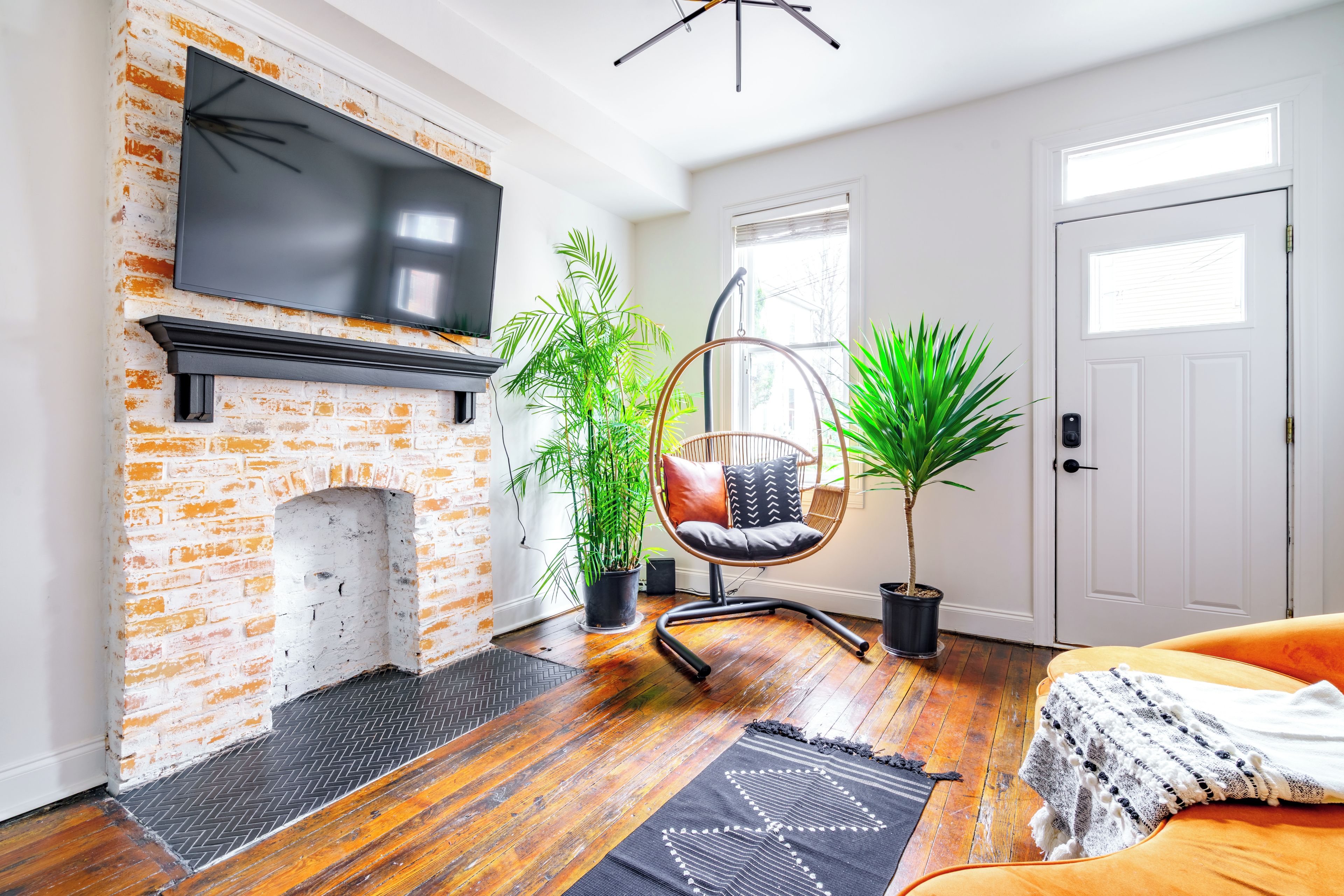 A living room with a brick fireplace, a hanging chair, potted plants, and a television.