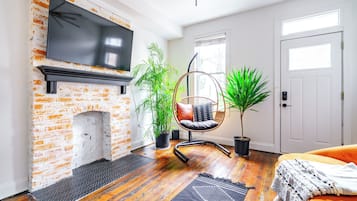 A living room with a brick fireplace, a hanging chair, potted plants, and a television.