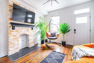 A living room with a brick fireplace, a hanging chair, potted plants, and a television.