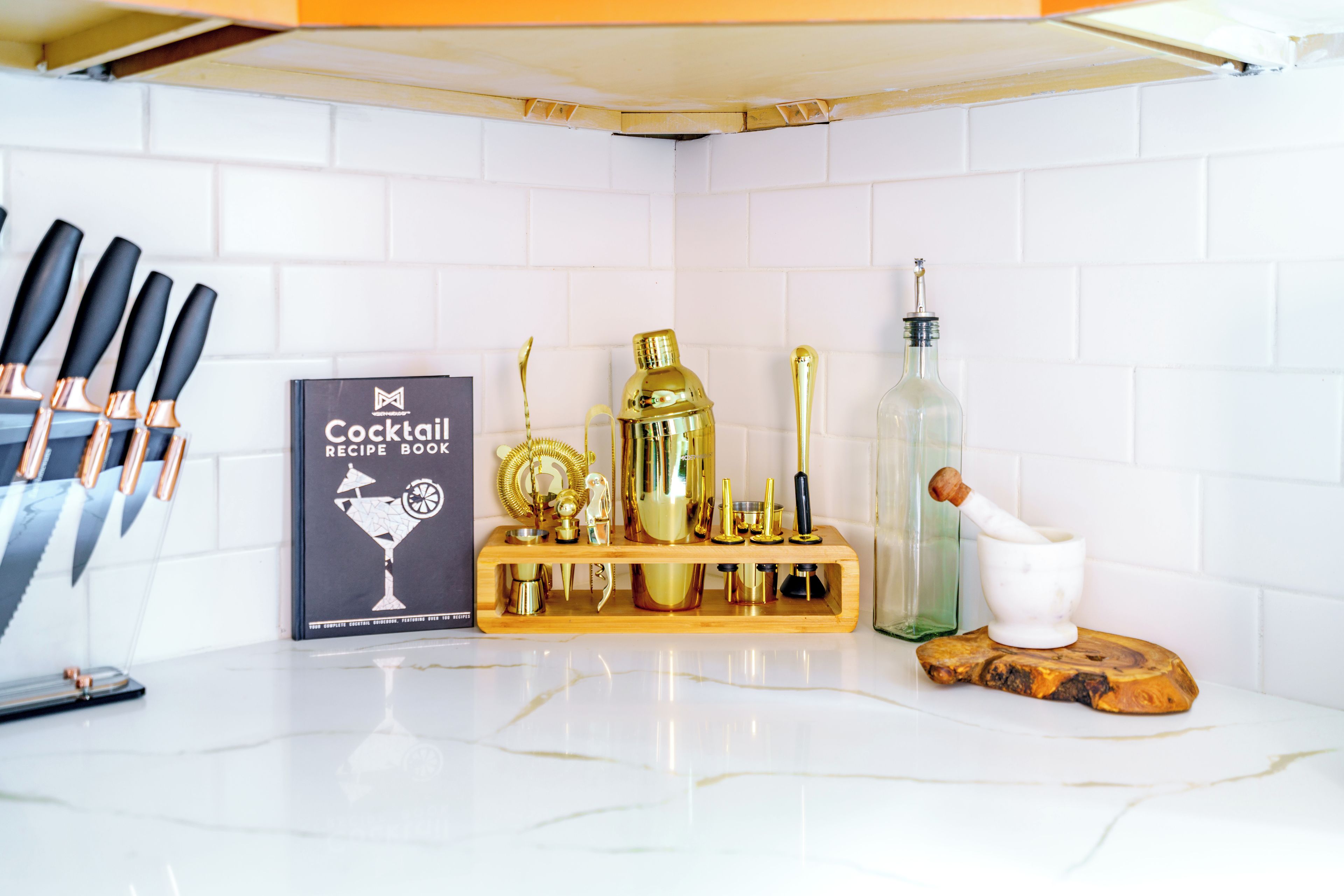 A kitchen counter with a cocktail recipe book, a wooden bar tool set, and a mortar and pestle.