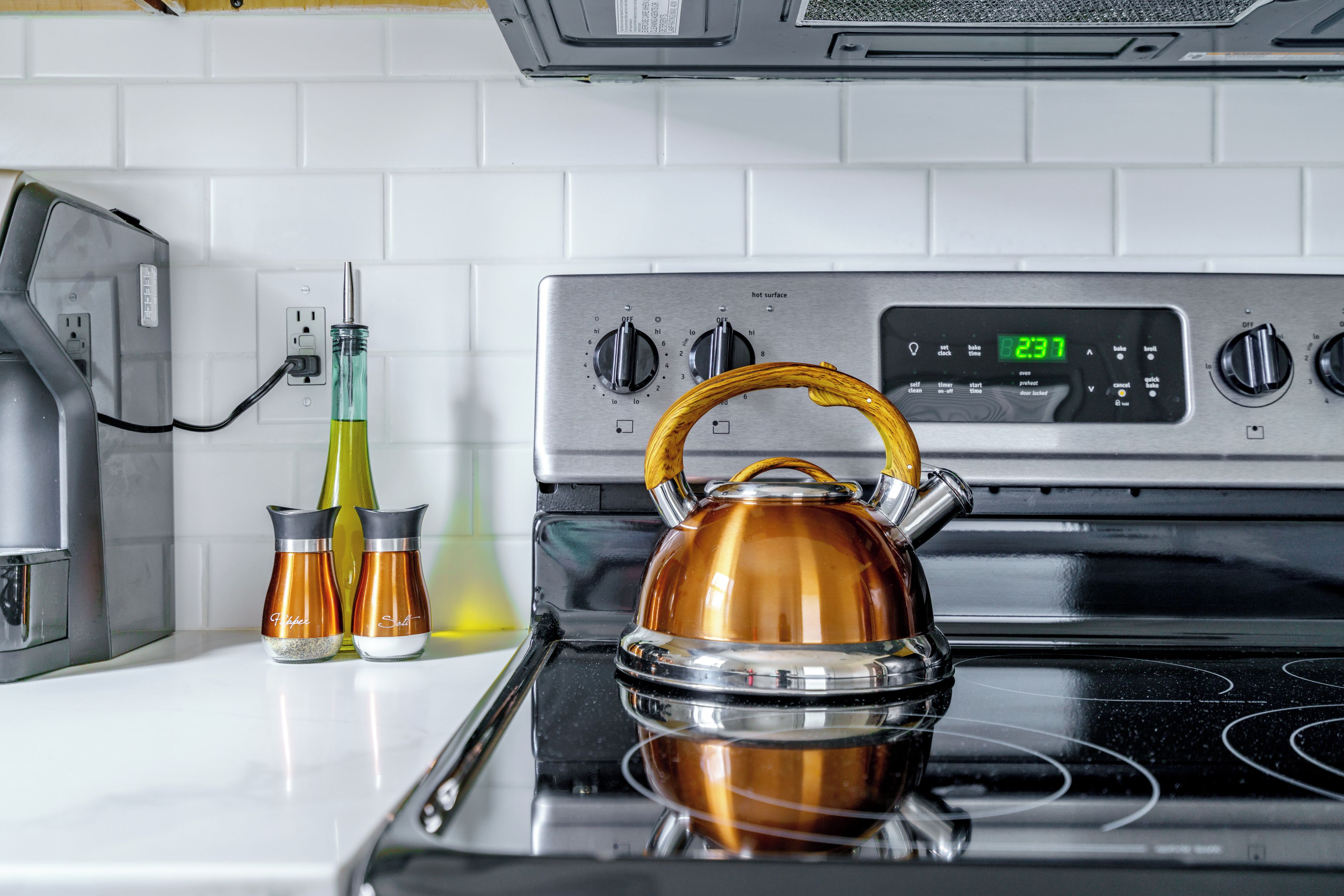 A kitchen with a stainless steel stove, two condiment bottles, and a kettle.