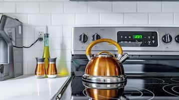 A kitchen with a stainless steel stove, two condiment bottles, and a kettle.