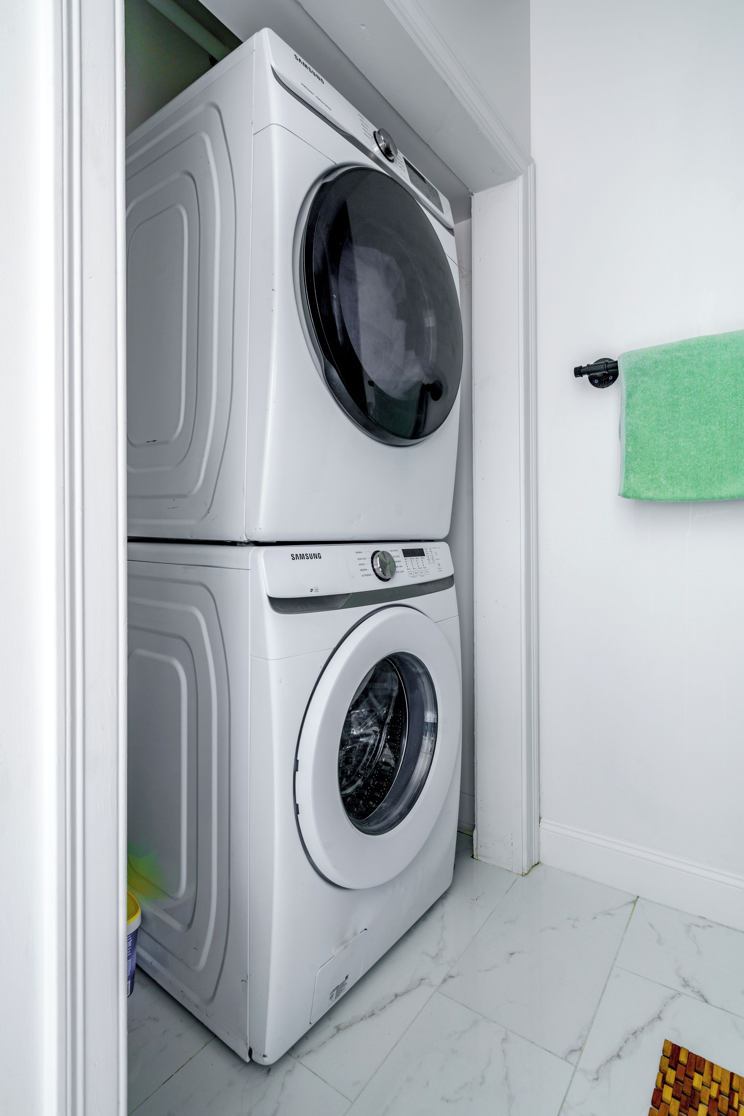 Una lavadora y secadora apiladas en un cuarto de lavado, con una toalla verde colgada en la pared.
