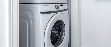 Een gestapelde wasmachine en droger in een wasserij, met een groene handdoek aan de muur.
