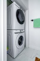 A stacked washer and dryer unit in a laundry room with a green towel hanging on the wall.