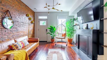 Una sala de estar moderna con pared de ladrillo, sofá de cuero, sillón colgante y un televisor grande.