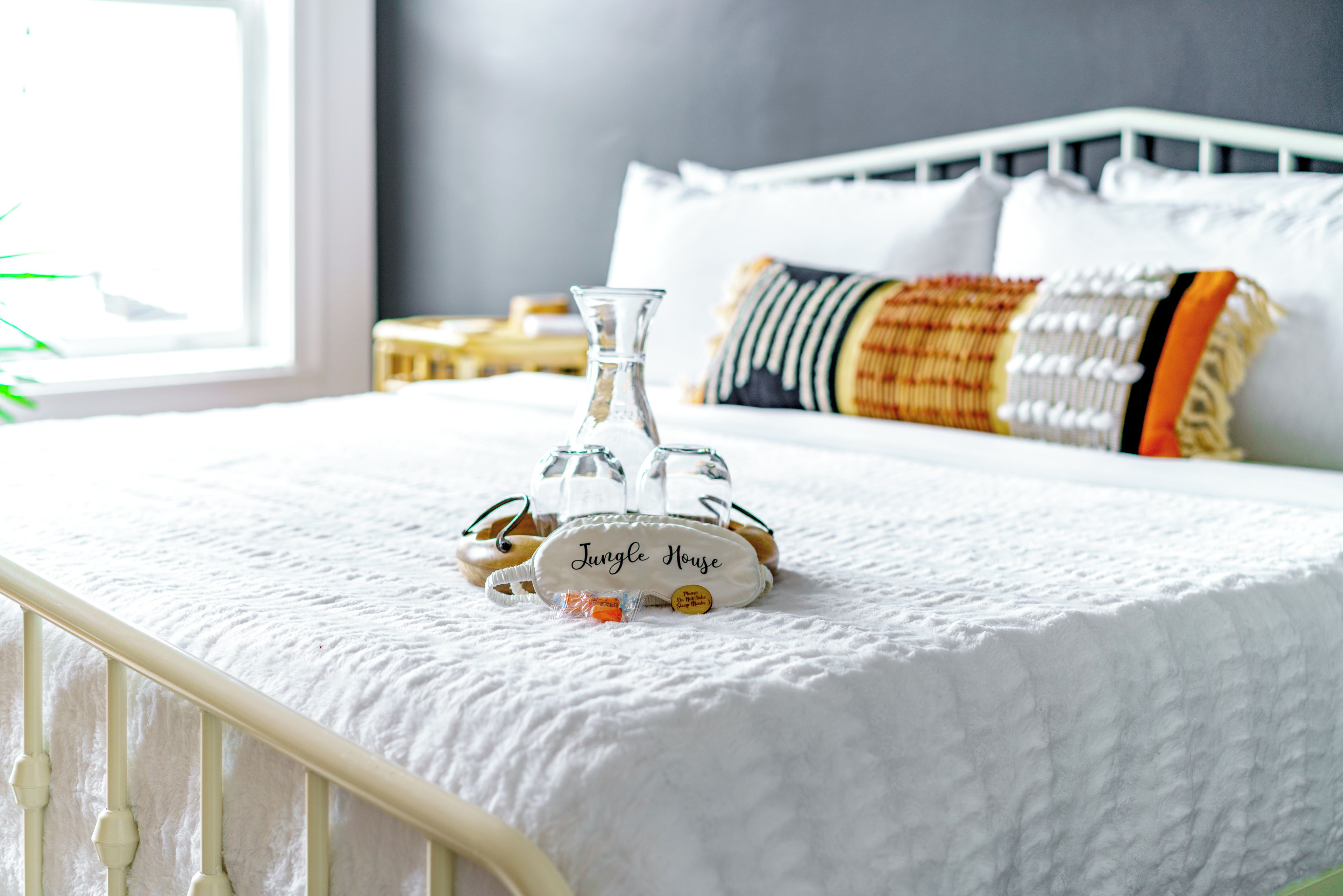 A bed with a white quilt, a glass bottle, and a small white bag labeled 'Jungle House' on it.