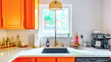 Una cocina con encimera blanca, pileta negra y armarios color naranja.