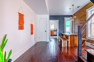 A hallway with wooden flooring, a staircase with a brick wall, and a kitchen visible in the background.
