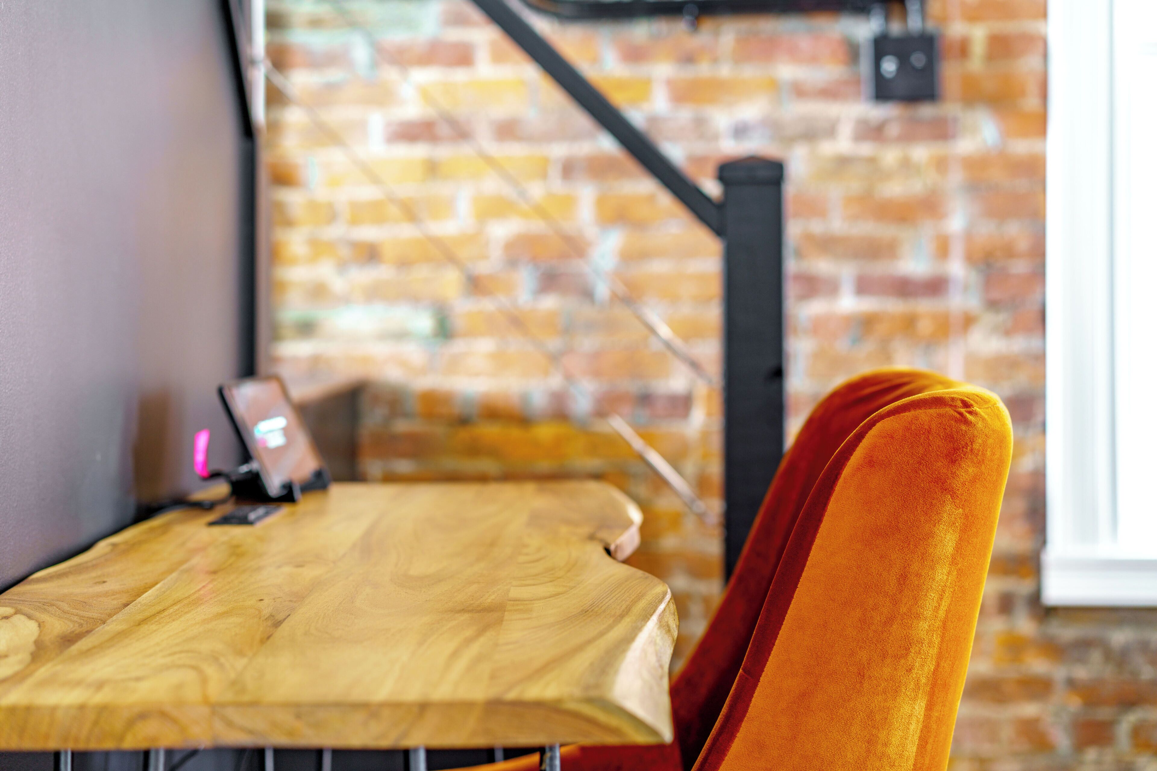 A wooden table with a laptop and a smartphone, a brick wall, and a window with a black metal structure.