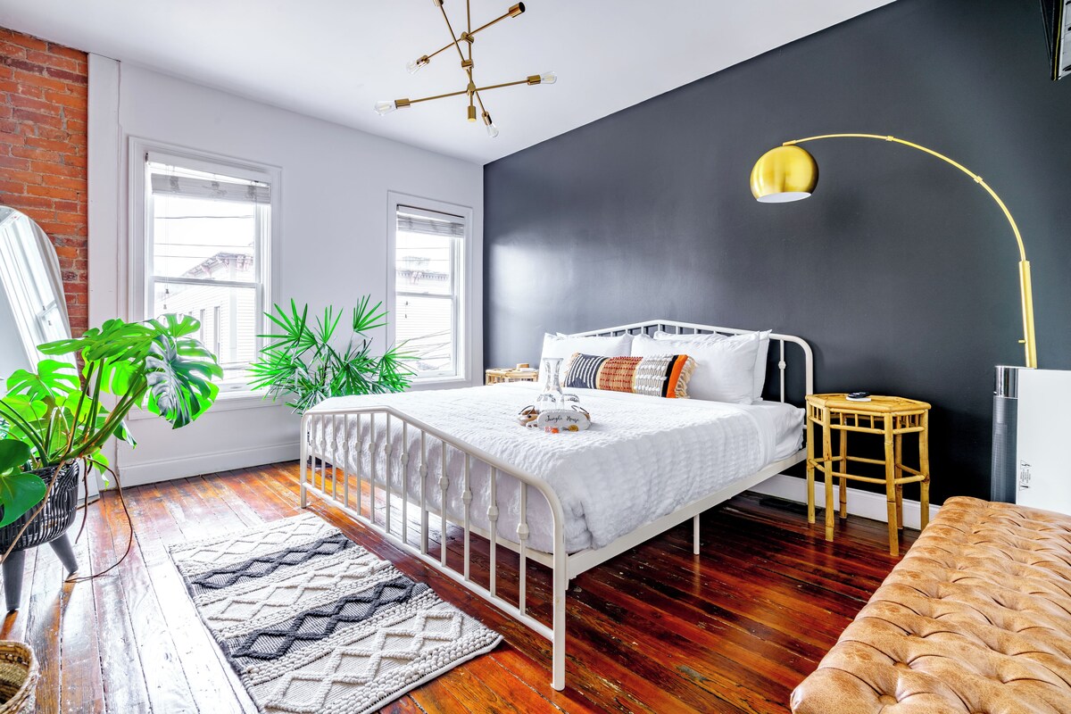 A bedroom with a bed, bedside table, lamp, and potted plants.