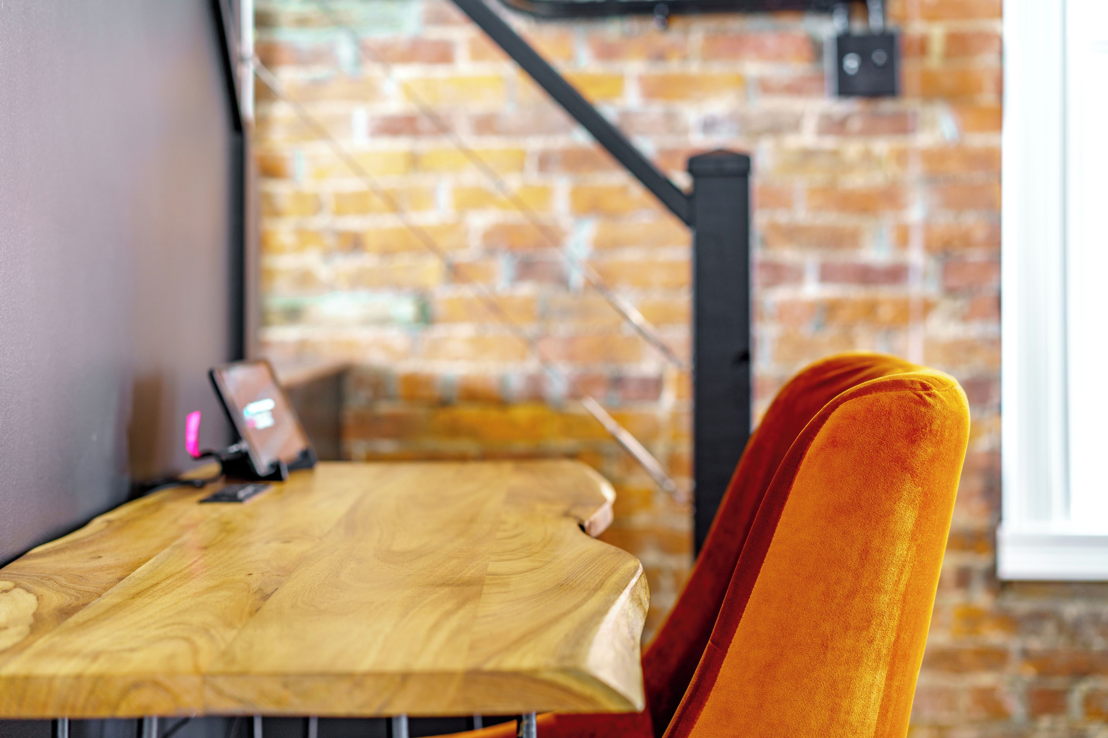 A wooden table with a laptop and a smartphone, a brick wall, and a window with a black metal structure.