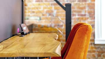 A wooden table with a laptop and a smartphone, a brick wall, and a window with a black metal structure.