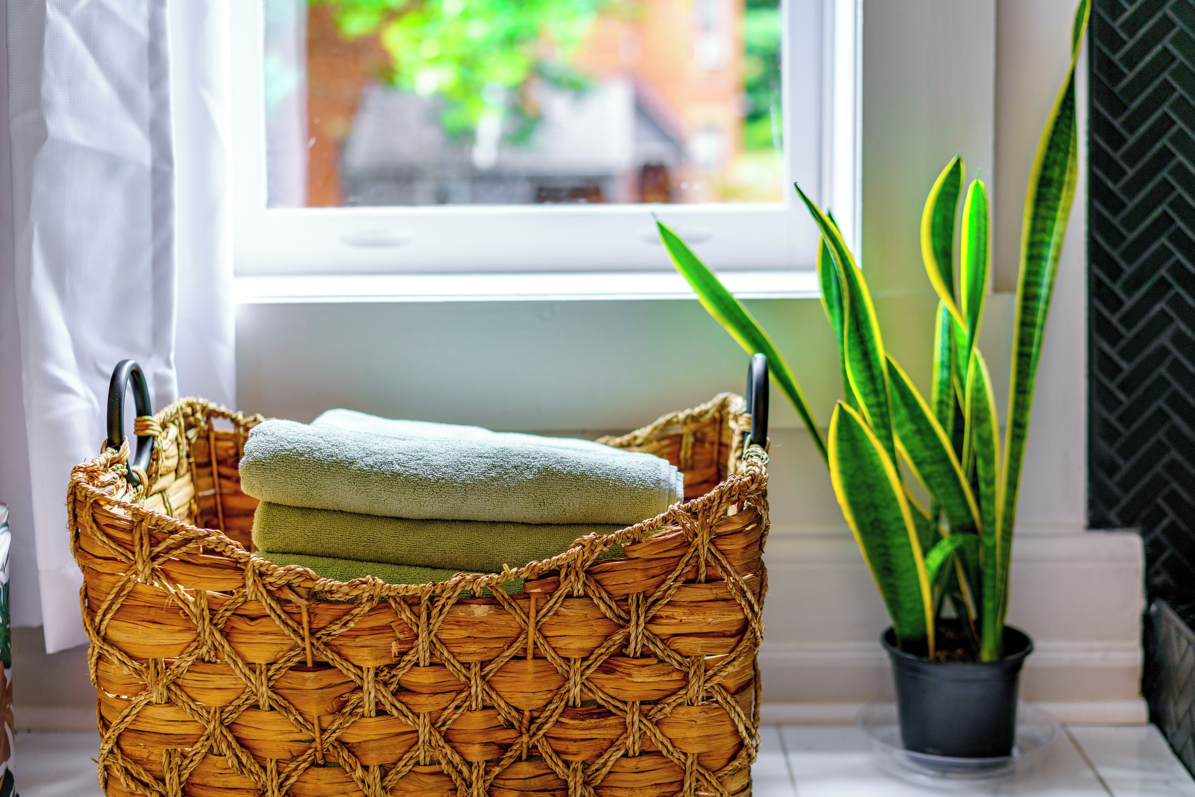 A wicker basket with towels, a potted plant, and a window with a view of buildings.