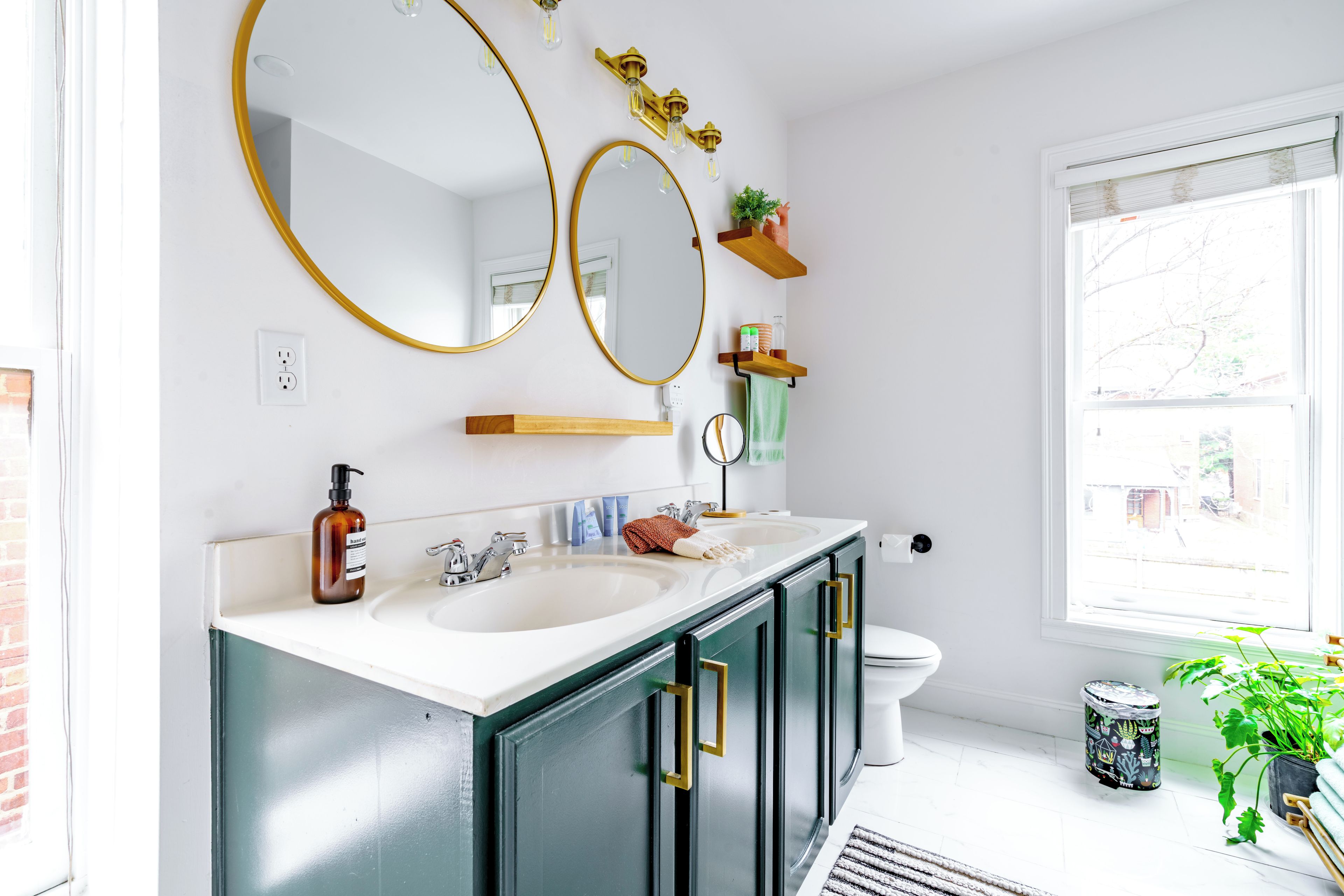 Une salle de bain moderne avec un double vasque, deux miroirs, des toilettes et une fenêtre.
