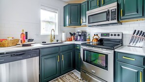 A kitchen with dark green cabinets, a stainless steel dishwasher, a microwave, an oven, and a coffee maker. - Jungle House Urban Lofts - Short North & Convention Center (Columbus)