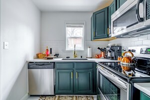 A compact kitchen with a dishwasher, stove, microwave, and green cabinets.