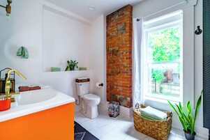A bathroom with a white sink, toilet, and a brick accent wall.
