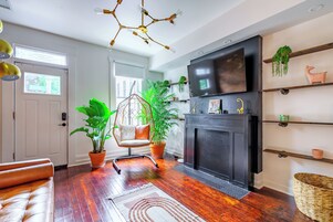 A living room with a fireplace, a TV, a hanging chair, and potted plants.